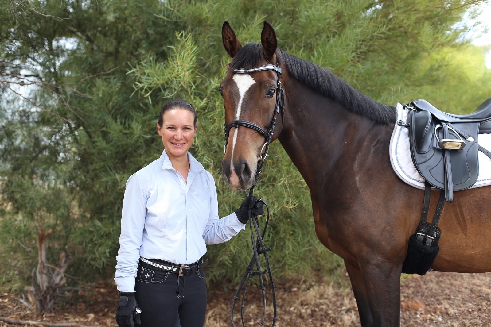 Katrin Kuenstler standing beside a saddled horse